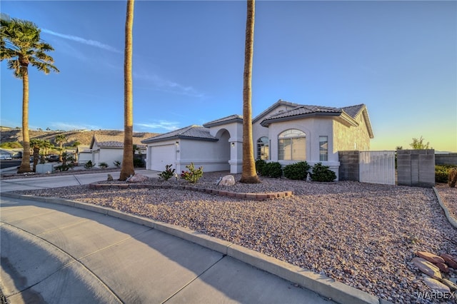 view of front of home featuring concrete driveway, stucco siding, a tile roof, a garage, and fence