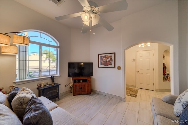 living room with a towering ceiling, baseboards, a ceiling fan, visible vents, and arched walkways