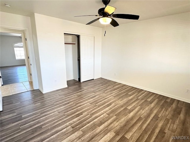 unfurnished bedroom with ceiling fan, baseboards, dark wood-type flooring, and a closet