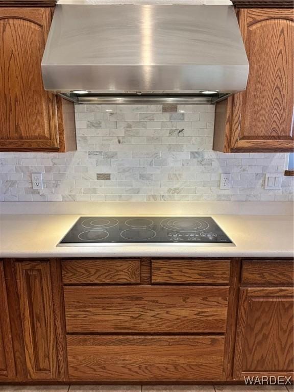 kitchen with black electric stovetop, tasteful backsplash, light countertops, and exhaust hood