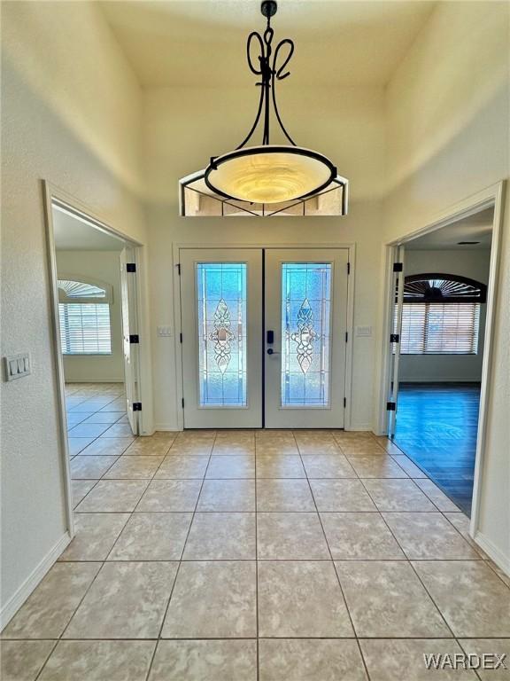 entryway featuring baseboards, a high ceiling, french doors, and light tile patterned floors