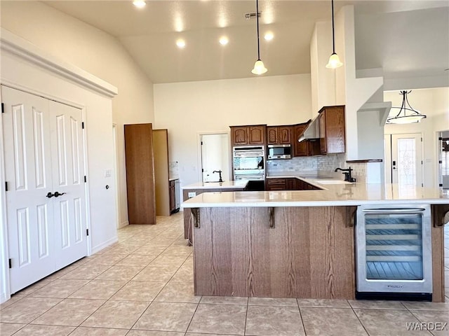 kitchen with under cabinet range hood, stainless steel appliances, light countertops, wine cooler, and high vaulted ceiling