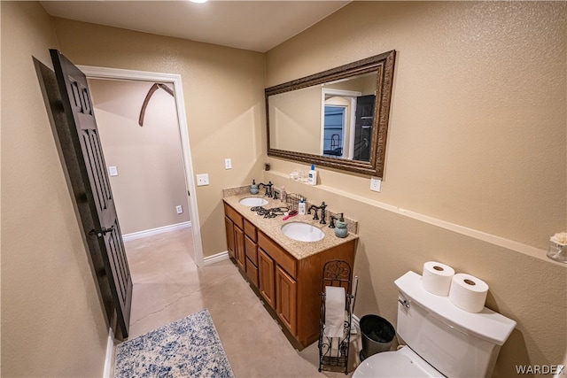 full bath with baseboards, a sink, toilet, and double vanity