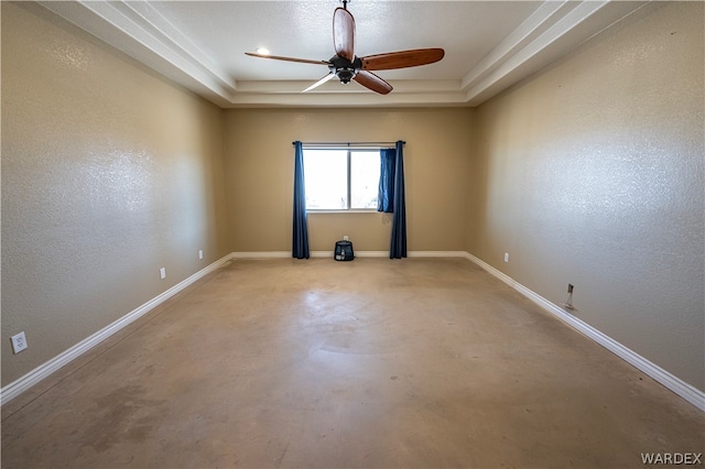 spare room with ceiling fan, a tray ceiling, concrete floors, and baseboards