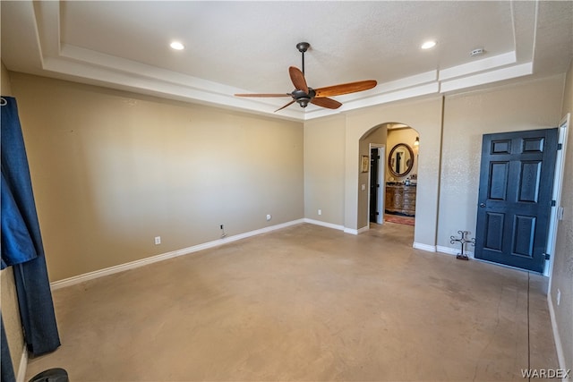 unfurnished room featuring a ceiling fan, a tray ceiling, arched walkways, and baseboards