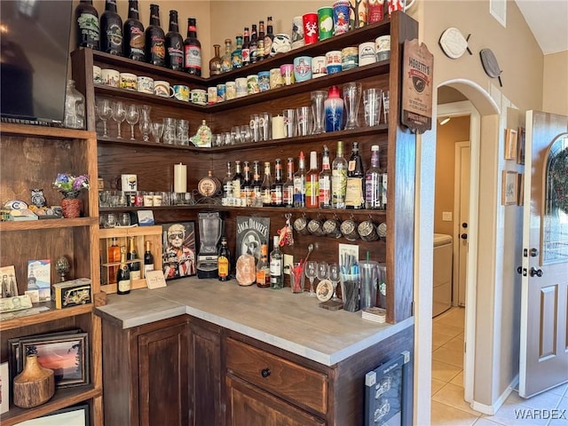 bar featuring light tile patterned floors, arched walkways, visible vents, a bar, and washer / dryer