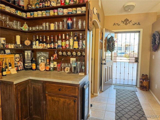 bar featuring a bar, light tile patterned floors, beverage cooler, and baseboards