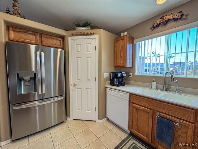 kitchen featuring a sink, light countertops, stainless steel refrigerator with ice dispenser, dishwasher, and brown cabinetry