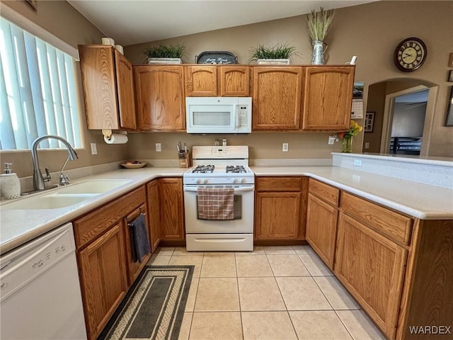 kitchen with light tile patterned flooring, a peninsula, white appliances, a sink, and light countertops