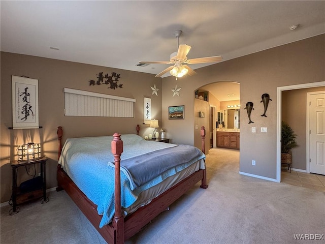 bedroom featuring arched walkways, light carpet, connected bathroom, ceiling fan, and baseboards