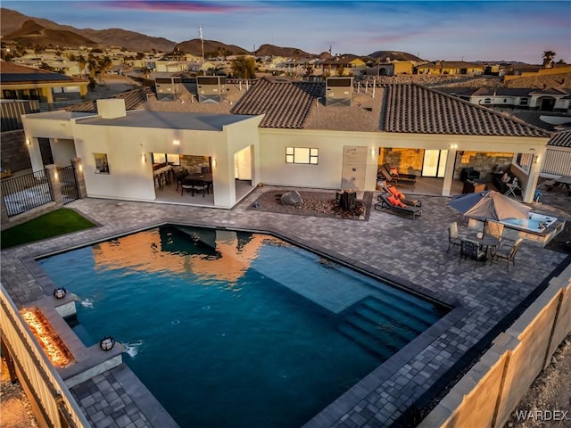 pool at dusk with an outdoor fire pit, a mountain view, fence, a residential view, and a fenced in pool