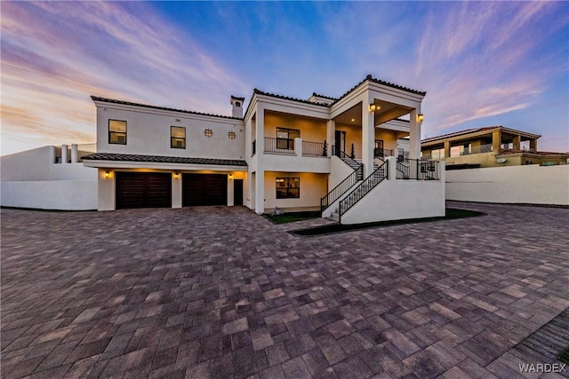 view of front of home with decorative driveway, a tile roof, stucco siding, an attached garage, and stairs