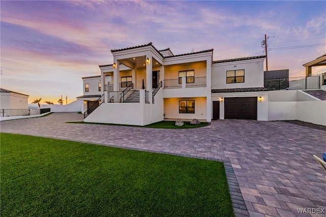 view of front of home featuring a balcony, a garage, decorative driveway, stucco siding, and a front yard