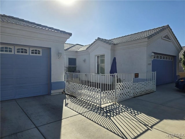 view of front facade featuring an attached garage, stucco siding, driveway, and a tiled roof