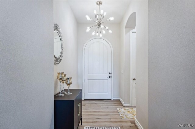 interior space with arched walkways, a textured wall, baseboards, light wood-style floors, and an inviting chandelier