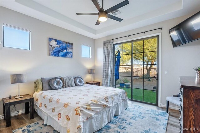 bedroom featuring wood finished floors, visible vents, baseboards, access to exterior, and a raised ceiling