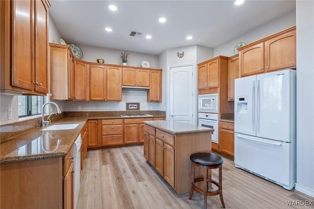 kitchen featuring white appliances, visible vents, dark stone counters, a center island, and a sink