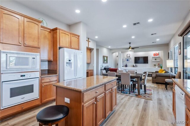 kitchen with white appliances, visible vents, open floor plan, a center island, and light wood finished floors