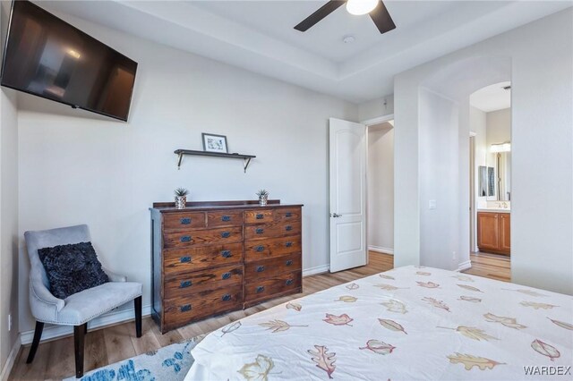 bedroom featuring light wood finished floors, baseboards, arched walkways, ceiling fan, and ensuite bathroom