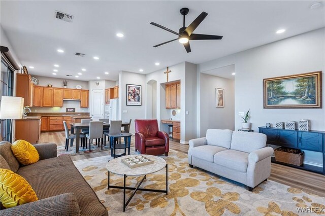 living room with light wood-style floors, arched walkways, and visible vents