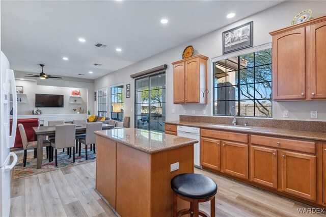 kitchen with white appliances, a kitchen island, open floor plan, light wood-type flooring, and a sink