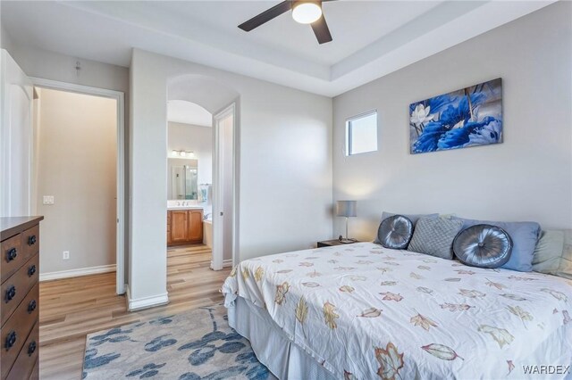 bedroom featuring arched walkways, light wood-style flooring, a ceiling fan, baseboards, and ensuite bath