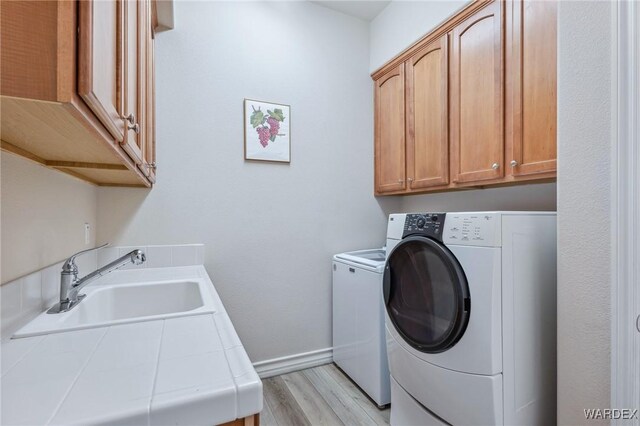 laundry room featuring washer and clothes dryer, cabinet space, light wood-style floors, a sink, and baseboards