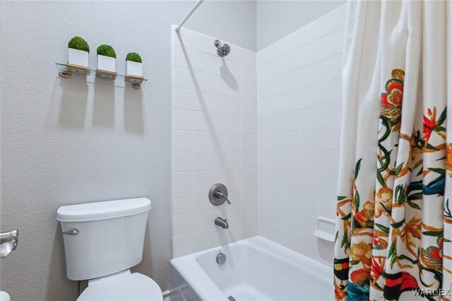 bathroom with shower / bath combination with curtain, a textured wall, and toilet