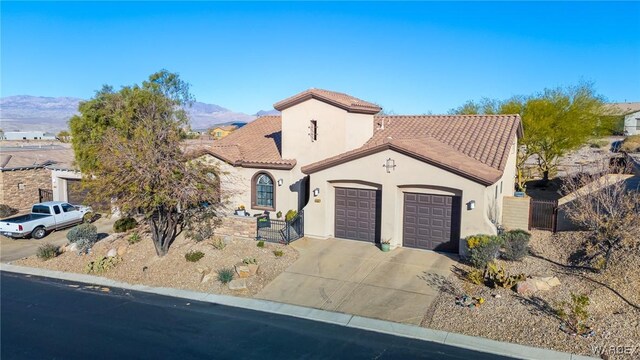 mediterranean / spanish-style home featuring a garage, concrete driveway, a tiled roof, a mountain view, and stucco siding