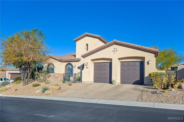 mediterranean / spanish home with an attached garage, a tiled roof, concrete driveway, and stucco siding