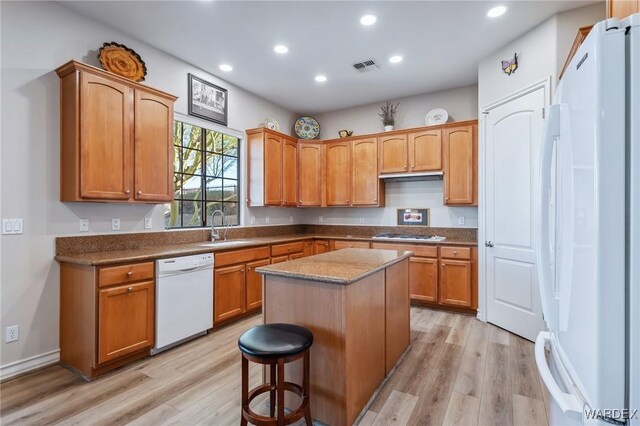 kitchen featuring white appliances, visible vents, a kitchen island, light wood-style floors, and a sink