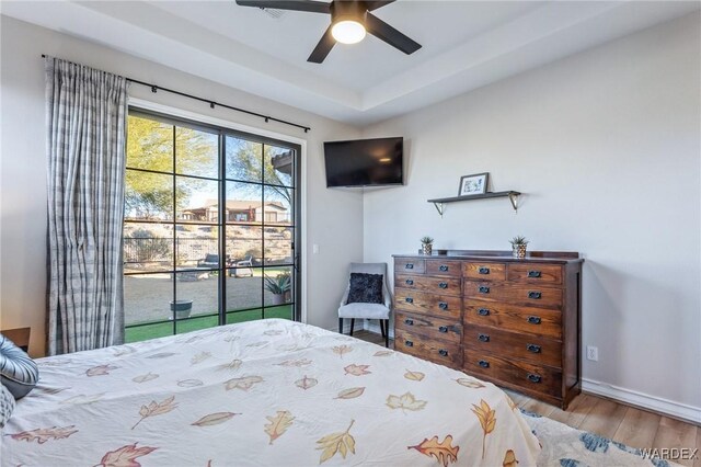 bedroom featuring baseboards, a ceiling fan, access to exterior, a tray ceiling, and light wood-type flooring