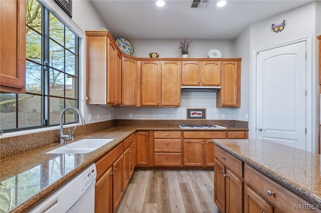 kitchen featuring light wood finished floors, visible vents, brown cabinetry, white dishwasher, and a sink