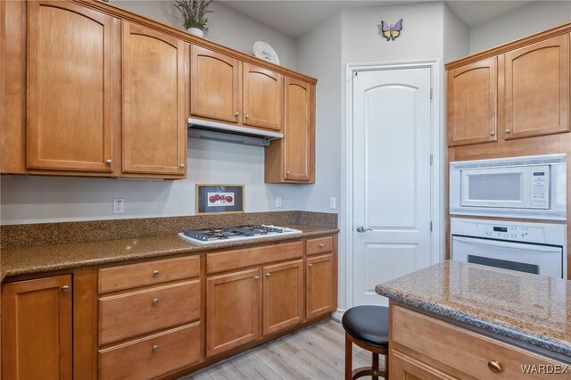 kitchen featuring light wood-style flooring, brown cabinetry, dark stone counters, white appliances, and extractor fan