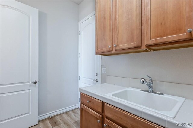 laundry area featuring light wood-style flooring, baseboards, and a sink