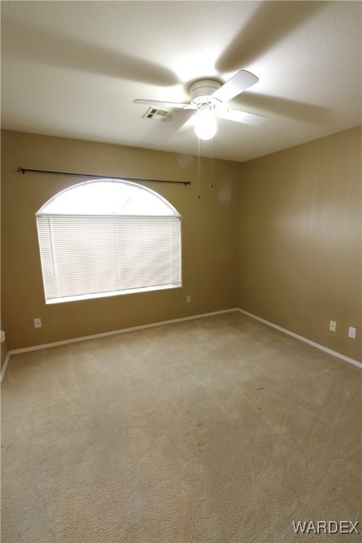 empty room featuring light carpet, ceiling fan, visible vents, and baseboards