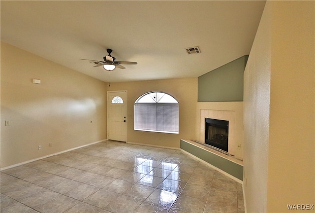 foyer entrance featuring baseboards, visible vents, a tiled fireplace, ceiling fan, and vaulted ceiling