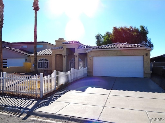 mediterranean / spanish-style house featuring driveway, a fenced front yard, a tiled roof, an attached garage, and stucco siding