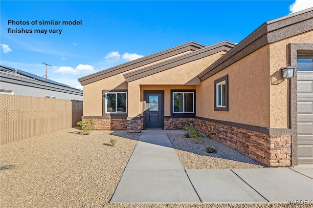 view of exterior entry with stone siding, fence, and stucco siding