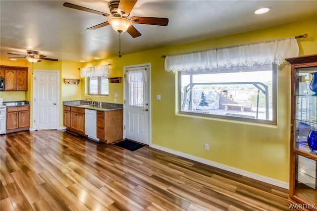 kitchen with light countertops, brown cabinetry, a sink, wood finished floors, and dishwasher