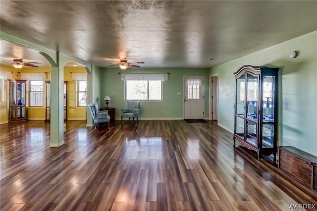 interior space featuring ceiling fan, baseboards, arched walkways, and dark wood finished floors