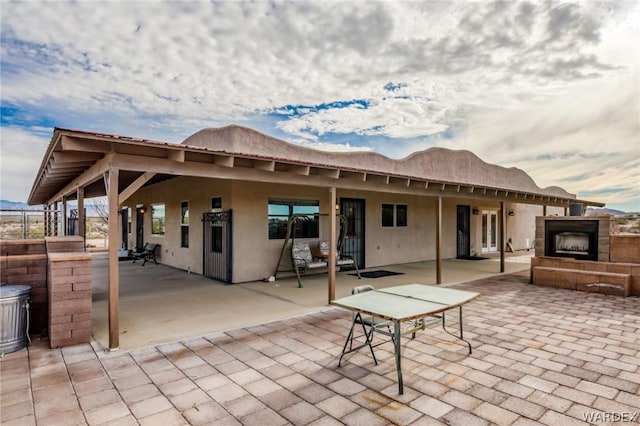 rear view of property featuring a patio, an outdoor stone fireplace, and stucco siding