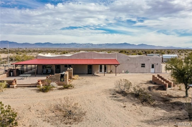 rear view of property featuring metal roof, an attached carport, a mountain view, and stucco siding