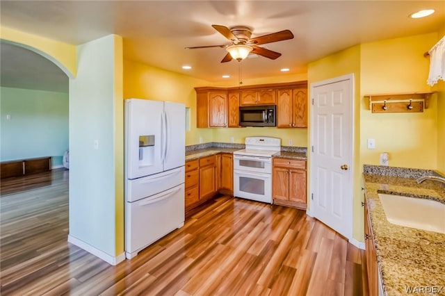 kitchen with brown cabinetry, white appliances, a sink, and wood finished floors