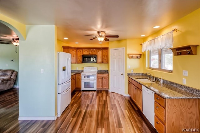 kitchen featuring white appliances, arched walkways, dark wood-style floors, ceiling fan, and light stone counters