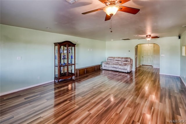 unfurnished living room with arched walkways, ceiling fan, wood finished floors, and baseboards