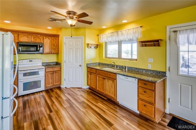 kitchen with white appliances, stone countertops, a healthy amount of sunlight, light wood-type flooring, and a sink