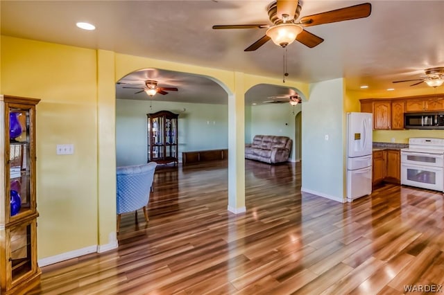 kitchen with white appliances, arched walkways, brown cabinets, wood finished floors, and light countertops