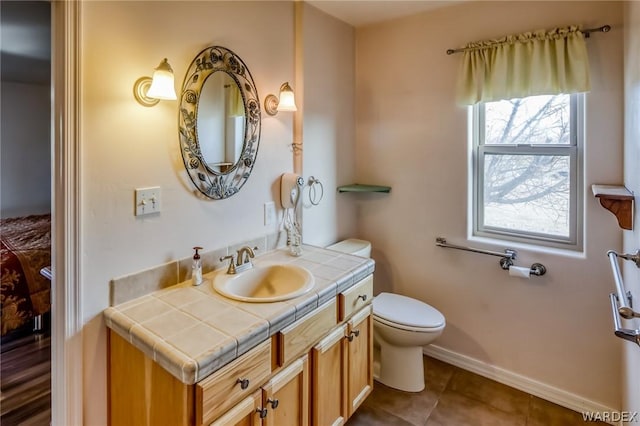 bathroom featuring toilet, tile patterned flooring, baseboards, and vanity