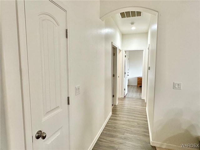 corridor featuring light wood-type flooring, baseboards, visible vents, and arched walkways